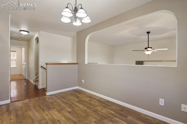 empty room with baseboards, ceiling fan with notable chandelier, arched walkways, and wood finished floors