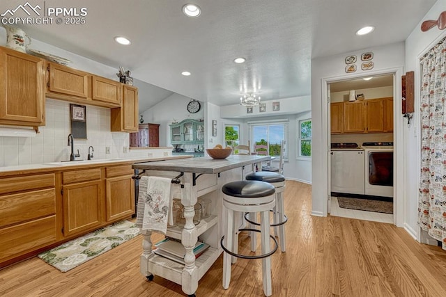16440 Eastonville Rd, Elbert, CO 80106 - kitchen with washer and clothes dryer, light wood-style floors, a breakfast bar area, decorative backsplash, and light countertops