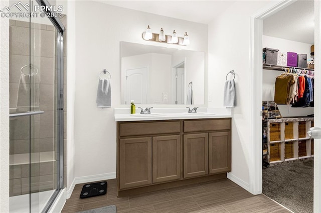 full bathroom featuring a walk in closet, double vanity, a stall shower, and a sink