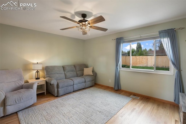 living room with baseboards, visible vents, wood finished floors, and a ceiling fan