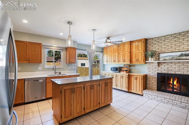 kitchen with a sink, stainless steel appliances, light tile patterned flooring, a brick fireplace, and a kitchen island