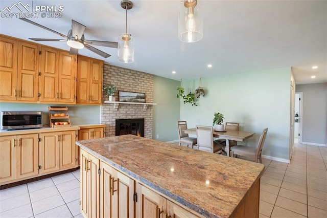 kitchen with a ceiling fan, a fireplace, light tile patterned flooring, and stainless steel microwave