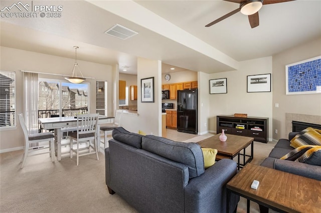 living area with a ceiling fan, light colored carpet, a tiled fireplace, visible vents, and baseboards