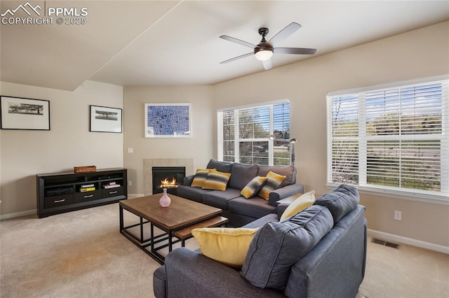 living room with ceiling fan, light carpet, a tiled fireplace, baseboards, and visible vents