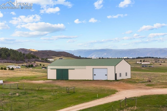 view of pole building with dirt driveway, a mountain view, fence, and a yard