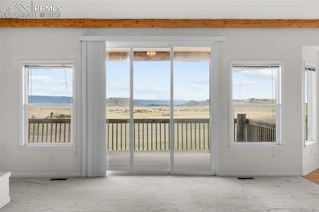 entryway featuring beamed ceiling, a mountain view, a healthy amount of sunlight, and carpet