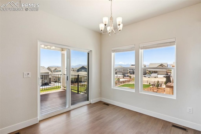 unfurnished dining area featuring plenty of natural light, a chandelier, baseboards, and wood finished floors