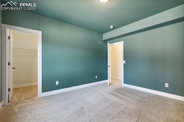 unfurnished bedroom with carpet floors, a walk in closet, and baseboards