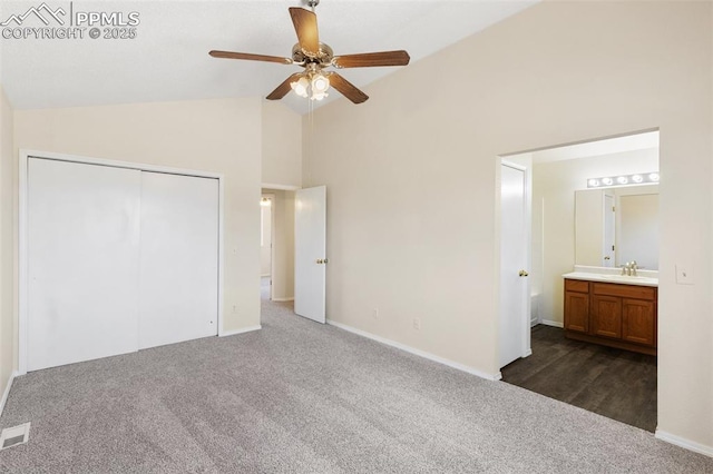 unfurnished bedroom with a sink, high vaulted ceiling, dark carpet, baseboards, and a closet