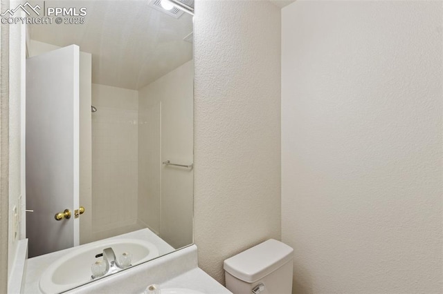 bathroom with a textured wall, walk in shower, vanity, toilet, and visible vents