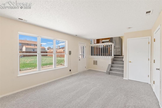 unfurnished living room with a healthy amount of sunlight, carpet flooring, a textured ceiling, and visible vents