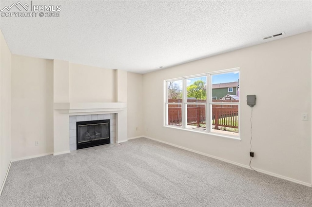 unfurnished living room with carpet floors, a textured ceiling, baseboards, a tile fireplace, and visible vents