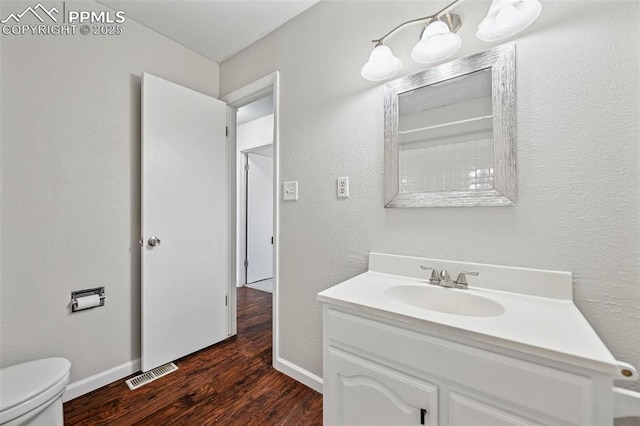 bathroom with vanity, visible vents, wood finished floors, toilet, and baseboards