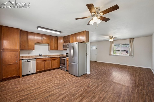 kitchen with a ceiling fan, brown cabinets, dark wood finished floors, a sink, and stainless steel appliances