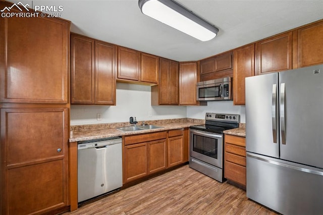 kitchen with brown cabinetry, a sink, light wood finished floors, and appliances with stainless steel finishes