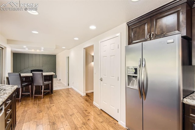 kitchen featuring dark brown cabinets, light stone counters, stainless steel fridge with ice dispenser, light wood-style floors, and recessed lighting