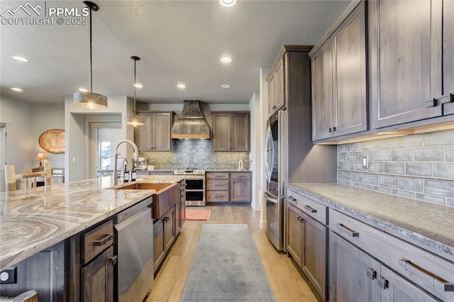 kitchen with light stone countertops, light wood-type flooring, tasteful backsplash, custom range hood, and appliances with stainless steel finishes
