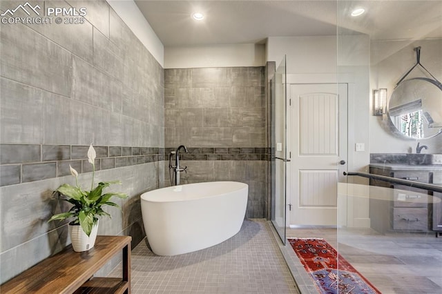 bathroom featuring tile patterned flooring, vanity, tile walls, and a soaking tub