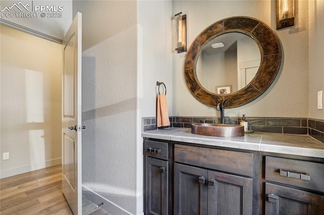 bathroom featuring baseboards, a textured wall, wood finished floors, and vanity