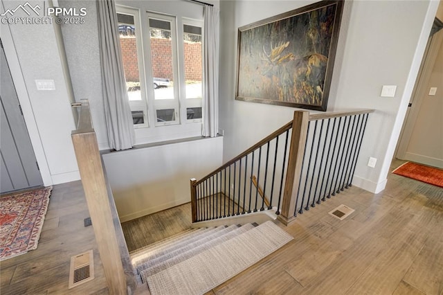 stairway with baseboards, wood finished floors, and visible vents