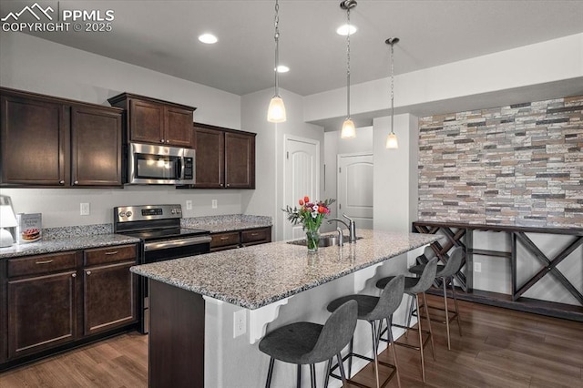 kitchen featuring light stone counters, a sink, dark wood finished floors, and appliances with stainless steel finishes