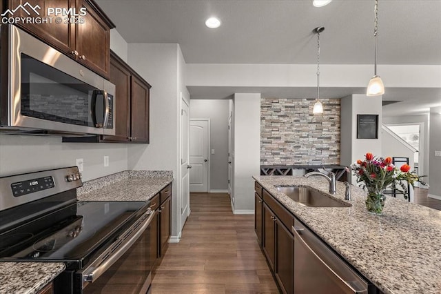kitchen with appliances with stainless steel finishes, light stone countertops, dark brown cabinets, a sink, and dark wood-style floors