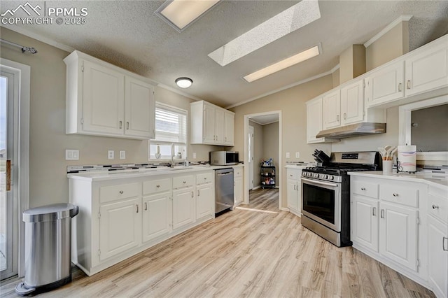 kitchen with under cabinet range hood, appliances with stainless steel finishes, ornamental molding, and lofted ceiling with skylight