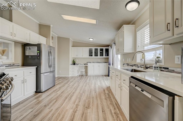 kitchen featuring appliances with stainless steel finishes, a sink, white cabinets, light wood finished floors, and ornamental molding