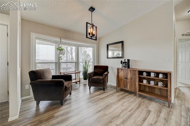 sitting room featuring an inviting chandelier, a textured ceiling, baseboards, wood finished floors, and vaulted ceiling