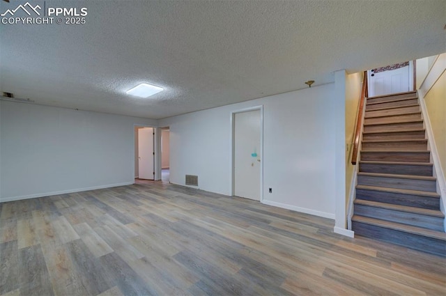 empty room featuring a textured ceiling, visible vents, wood finished floors, stairway, and baseboards