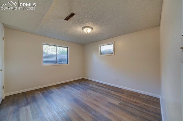 empty room with visible vents, a textured ceiling, wood finished floors, and a wealth of natural light
