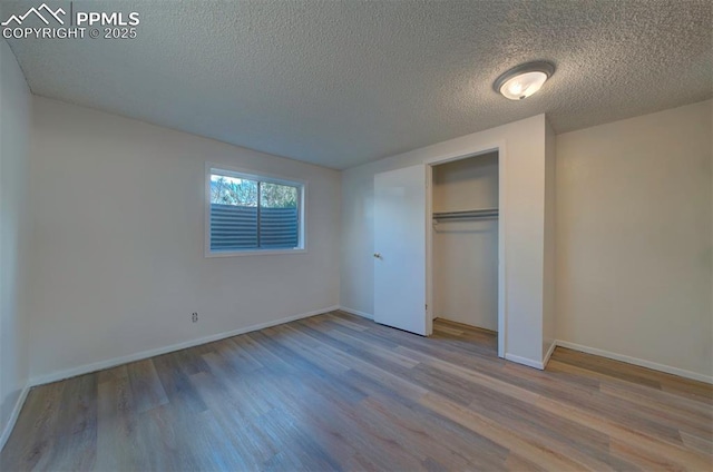 unfurnished bedroom with a textured ceiling, baseboards, a closet, and wood finished floors