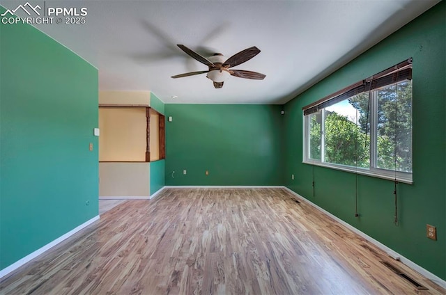 empty room with baseboards, a ceiling fan, wood finished floors, and visible vents
