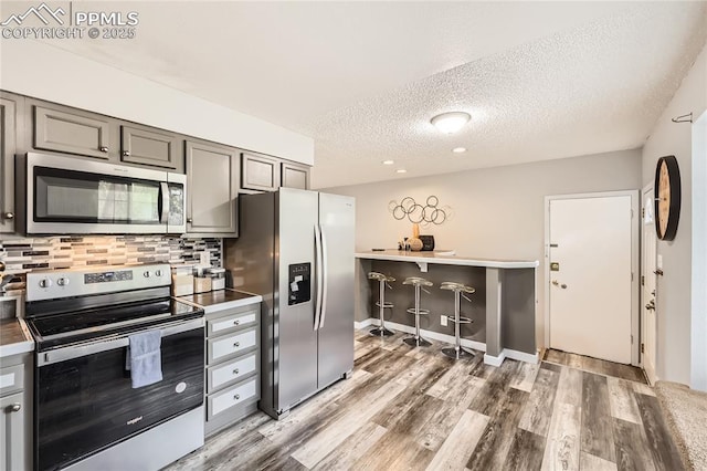 kitchen with light wood-style flooring, a textured ceiling, gray cabinetry, appliances with stainless steel finishes, and decorative backsplash