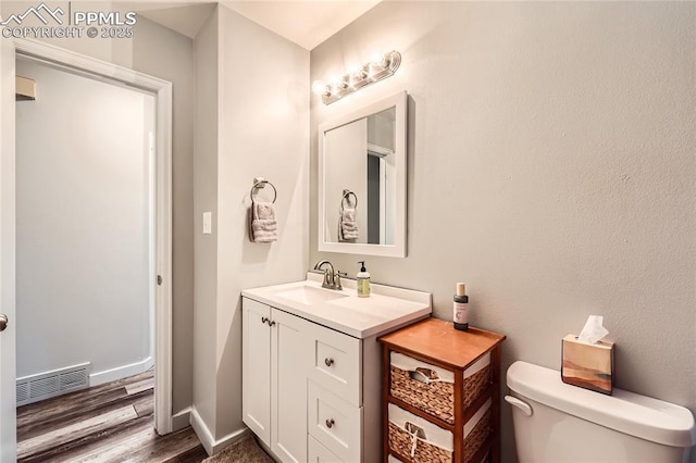 half bathroom with toilet, wood finished floors, visible vents, baseboards, and vanity