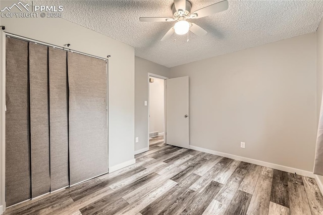unfurnished bedroom featuring wood finished floors, a ceiling fan, a closet, a textured ceiling, and visible vents