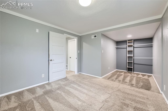 unfurnished bedroom featuring carpet, crown molding, a textured ceiling, visible vents, and baseboards