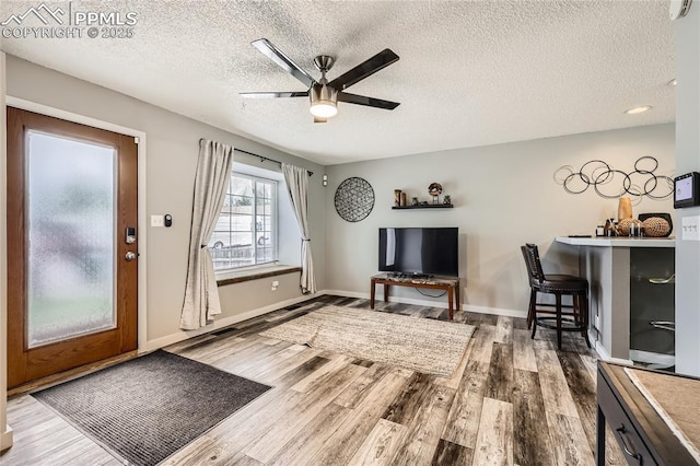 interior space with a ceiling fan, baseboards, a textured ceiling, and wood finished floors