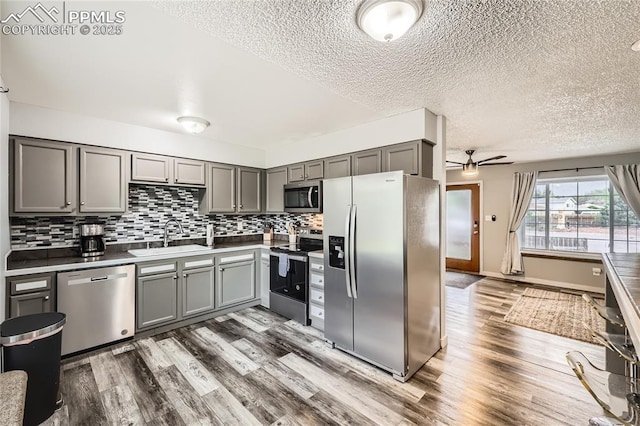 kitchen featuring a sink, gray cabinets, wood finished floors, a ceiling fan, and appliances with stainless steel finishes