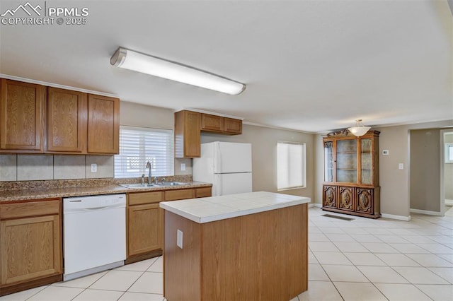 kitchen featuring a center island, brown cabinets, a sink, light tile patterned floors, and white appliances