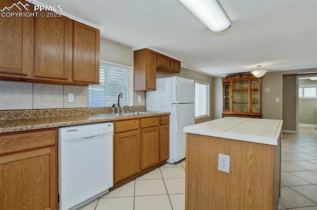 kitchen with a sink, white appliances, brown cabinetry, light tile patterned floors, and a kitchen island