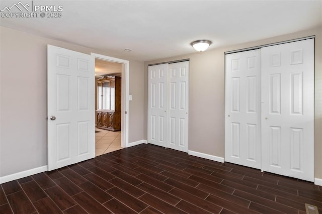 unfurnished bedroom with baseboards, two closets, wood finished floors, and visible vents