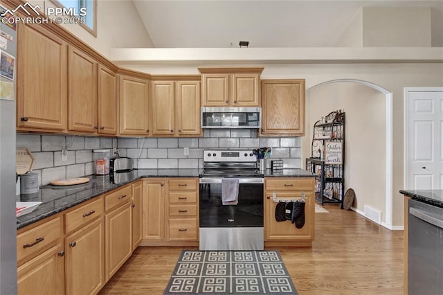 kitchen featuring dark stone counters, appliances with stainless steel finishes, backsplash, and light wood finished floors