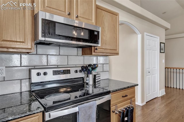 kitchen featuring light brown cabinetry, appliances with stainless steel finishes, dark stone countertops, wood finished floors, and tasteful backsplash