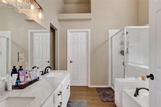 full bathroom featuring double vanity, a bath, a shower stall, wood finished floors, and a sink