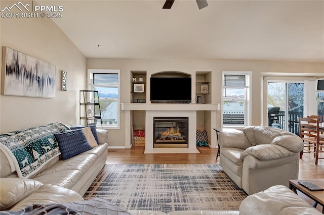 living area featuring a fireplace with flush hearth, a ceiling fan, wood finished floors, and a wealth of natural light