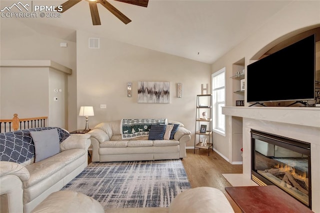 living area with a ceiling fan, wood finished floors, vaulted ceiling, a high end fireplace, and visible vents