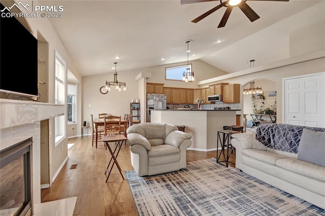 living room featuring light wood finished floors, a fireplace, arched walkways, ceiling fan with notable chandelier, and vaulted ceiling