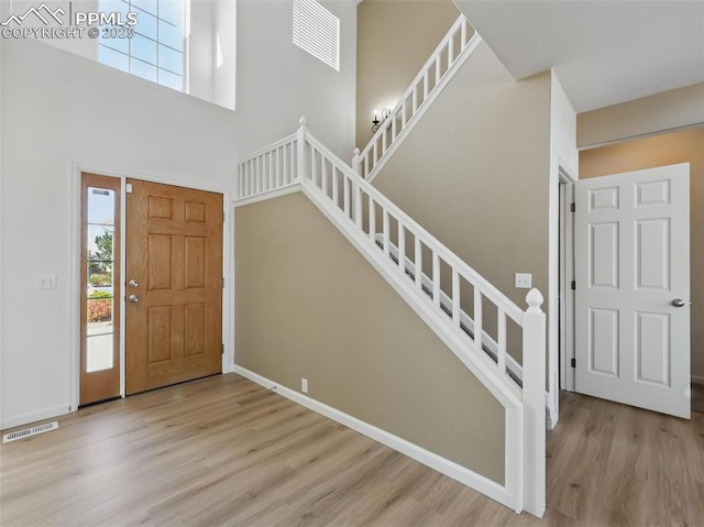 entrance foyer featuring stairs, baseboards, wood finished floors, a towering ceiling, and visible vents