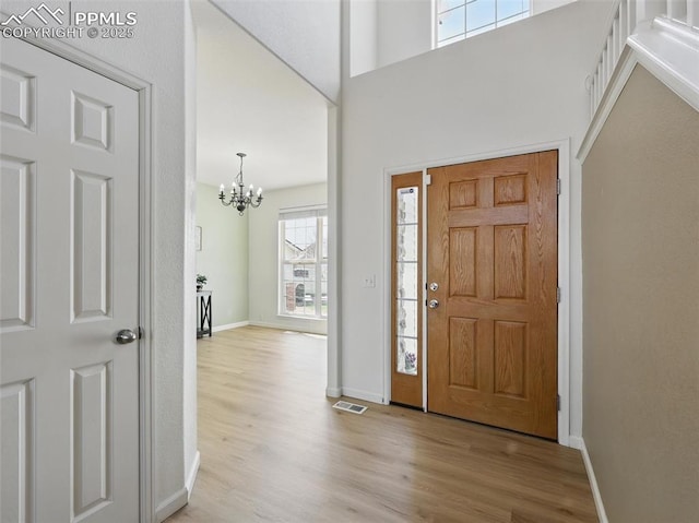 foyer entrance with an inviting chandelier, visible vents, wood finished floors, baseboards, and a high ceiling